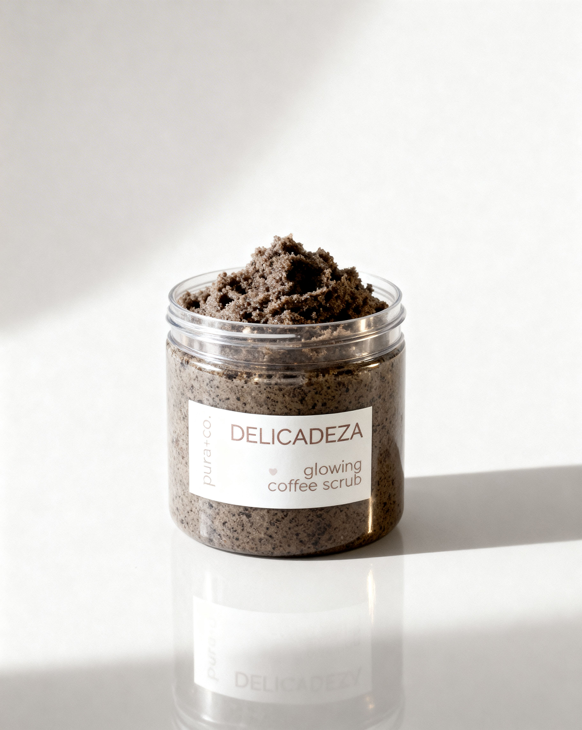 Pura+Co | The Delicadeza Coffee Scrub jar sits on a solid surface | Exfoliante Natural | Oatmeal Honey Scent | Handmade Skin Care | Puerto Rico