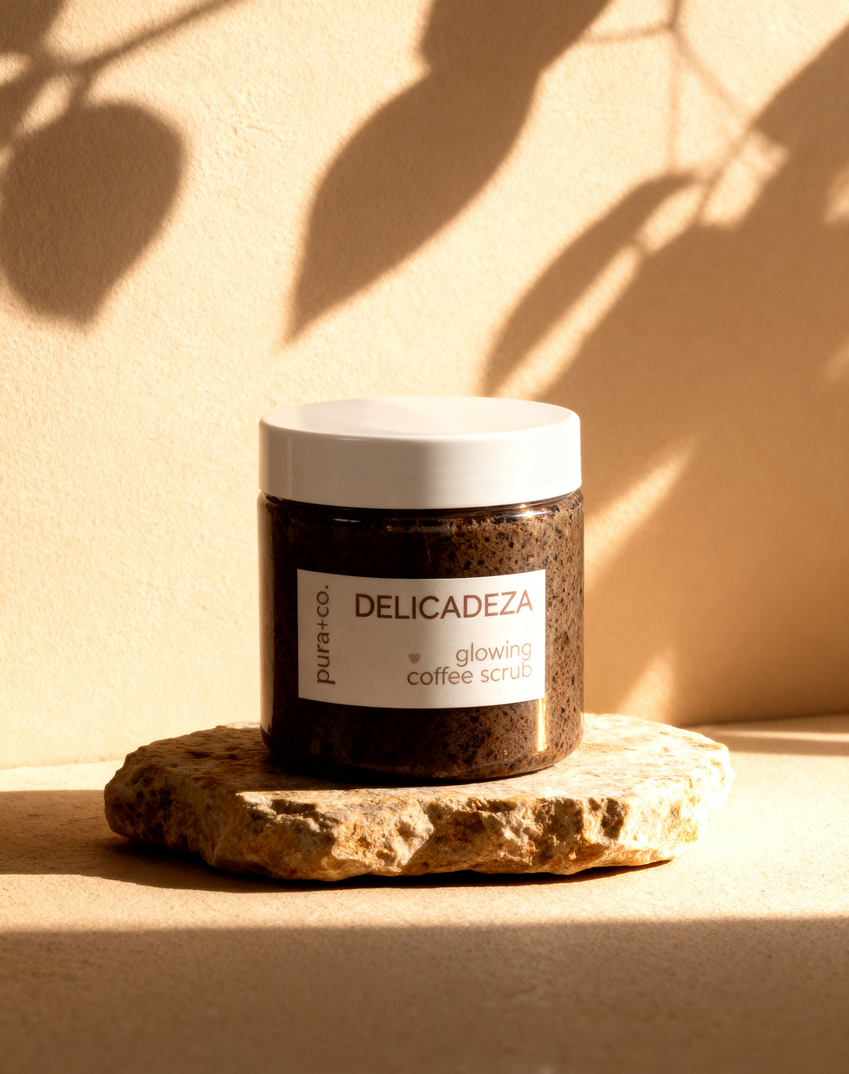Pura+Co | The Delicadeza Coffee Scrub jar sits on a stone surface | Exfoliante Natural | Oatmeal Honey Scent | Handmade Skin Care | Puerto Rico
