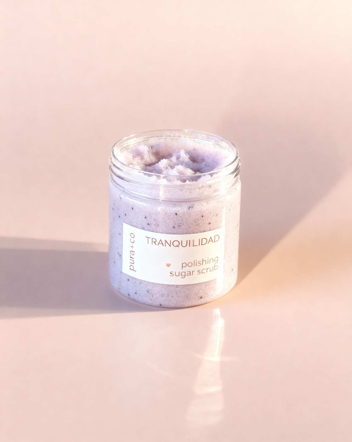Pura+Co | Tranquilidad Sugar Scrub sits on a solid surface with the cap open showcasing the texture | Exfoliante Natural |  Lavender Vanilla Scent | Handmade Skin Care | Puerto Rico